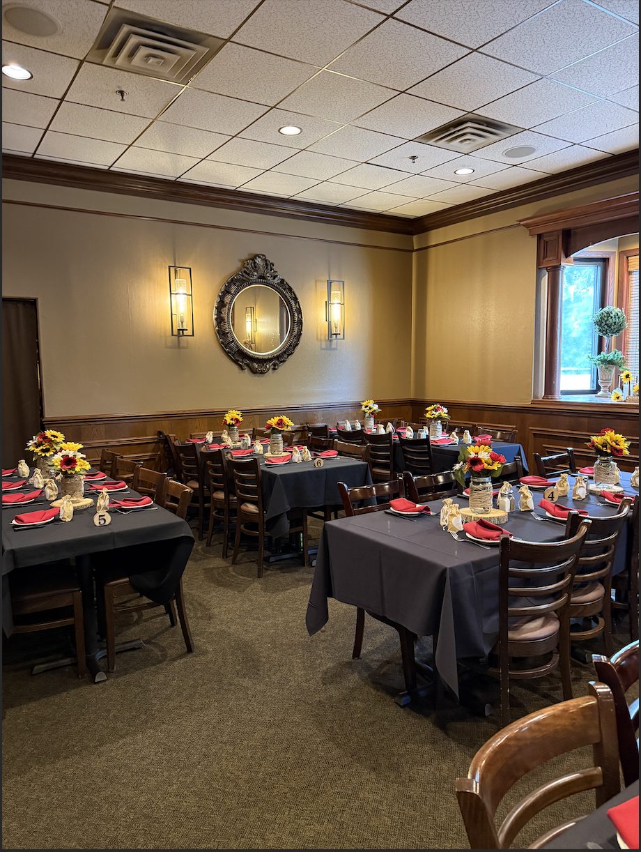 A private dining room with tables in dark linens, red napkins, sunflower centerpieces and a gilt mirror on the wall.