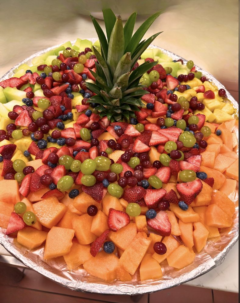A large fresh fruit platter of cantaloupe, honeydew, pineapple, strawberries, grapes and blueberries arranged around a pineapple crown.