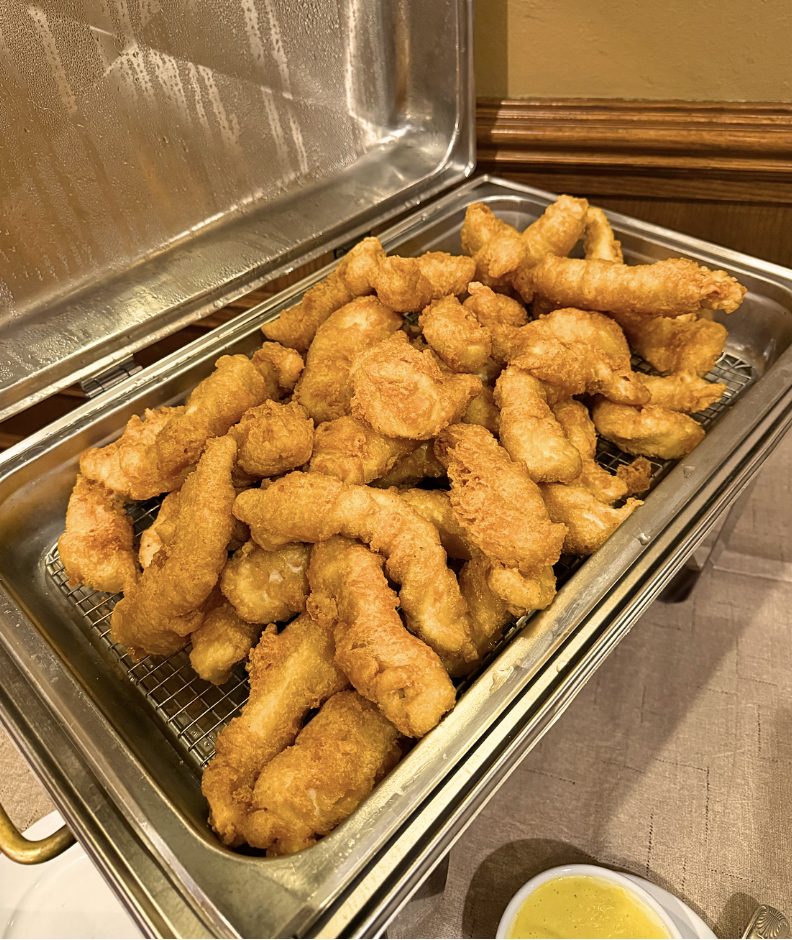 A chafing dish piled with golden fried chicken tenders and a bowl of honey mustard.
