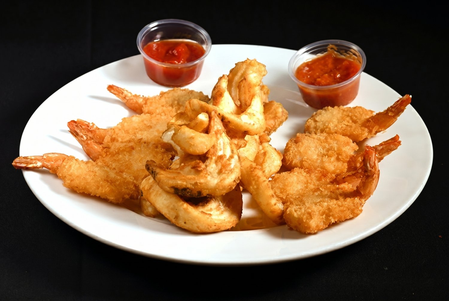 Plate of lightly breaded butterflied Gulf shrimp, deep fried golden, with two cups of homemade cocktail sauce.