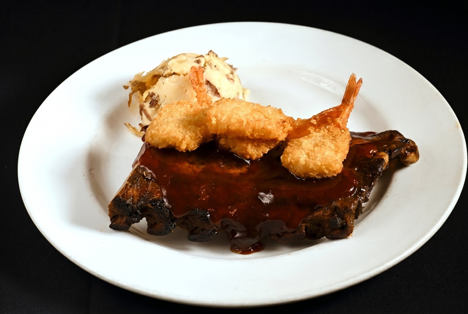 Half slab of BBQ baby back ribs glazed in house barbecue sauce, topped with breaded fried shrimp and served with garlic mashed potatoes.