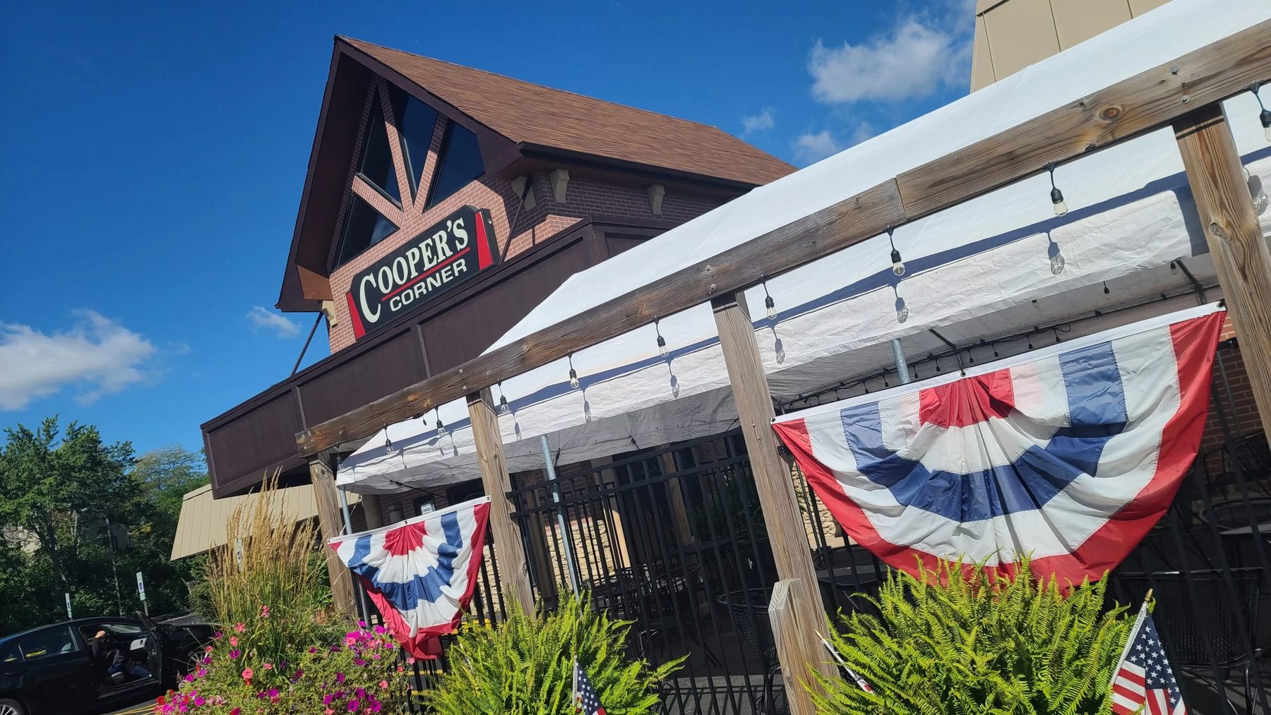 The Cooper's Corner sign above the covered patio, decorated with red, white and blue bunting on a clear summer day.